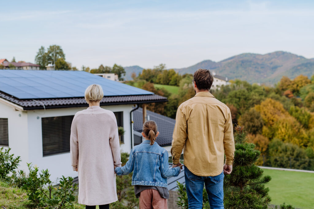 Famille qui regarde ses panneaux photovoltaïques sur le toit de leur maison. Autonomie avec le stockage virtuel de l'énergie proposé par Isowatt.