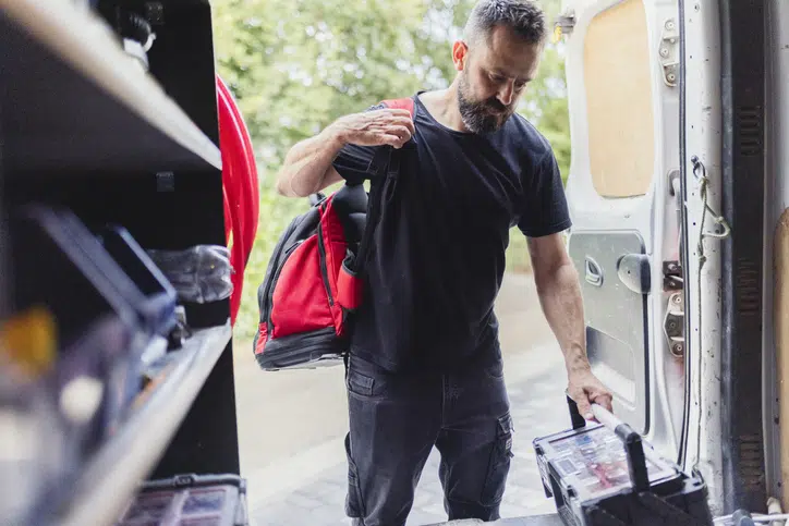After successfully installing the heat pump, male engineer brings the tool bag into his vehicle