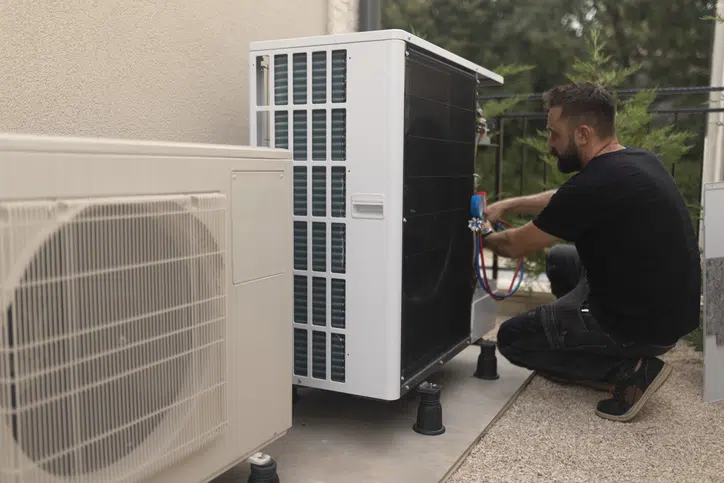 The man installs and adjusts the heat pump in the yard. The advantages of using heat pumps in homes are energy efficiency, cost savings